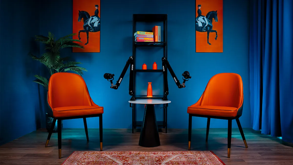 Two orange chairs facing each other against a deep blue wall, with microphones on boom arms